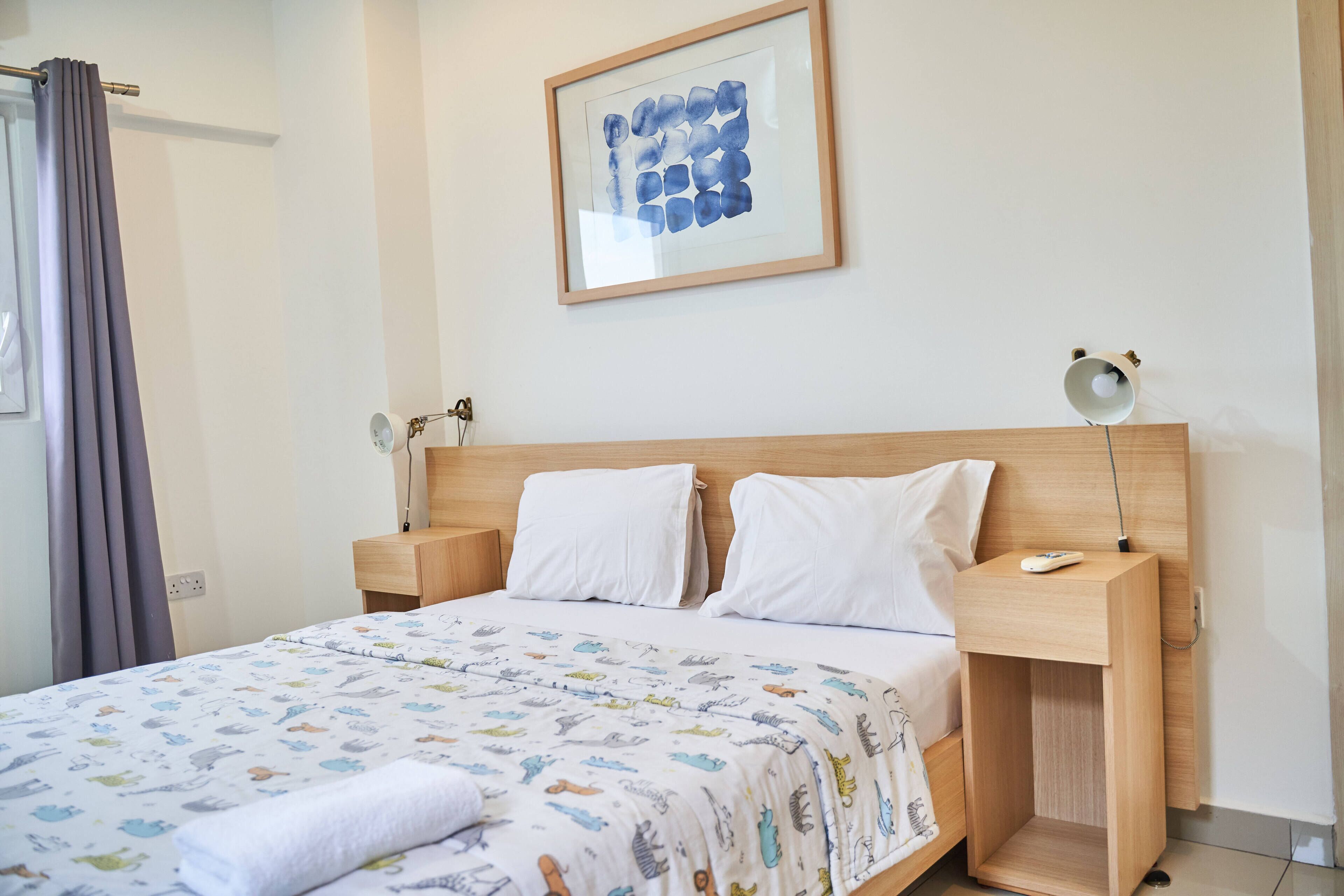 Un lit bien fait, recouvert d’une couverture à motifs, une table de chevet avec une lampe et une œuvre d’art encadrée accrochée au mur.