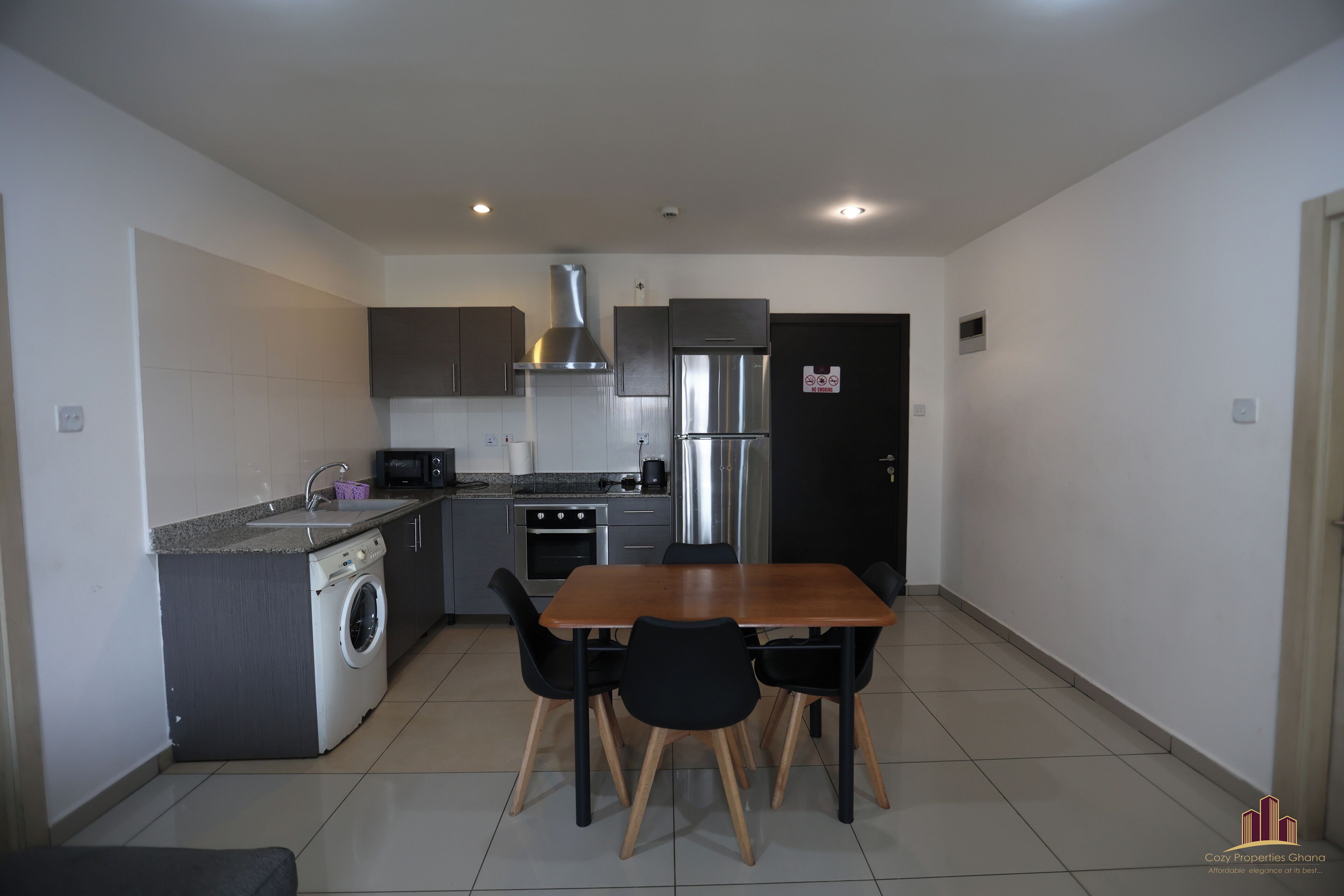 A compact kitchen with a washing machine, microwave, stove, and stainless steel refrigerator.