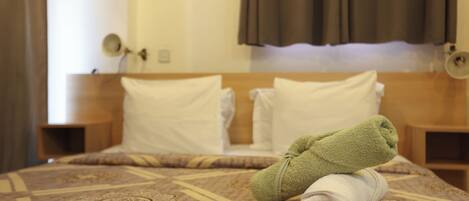 A neatly made bed with a patterned bedspread, two pillows, and a rolled towel on the bed.