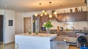 Cocina moderna con una isla central, electrodomésticos de acero inoxidable y una lámpara colgante.