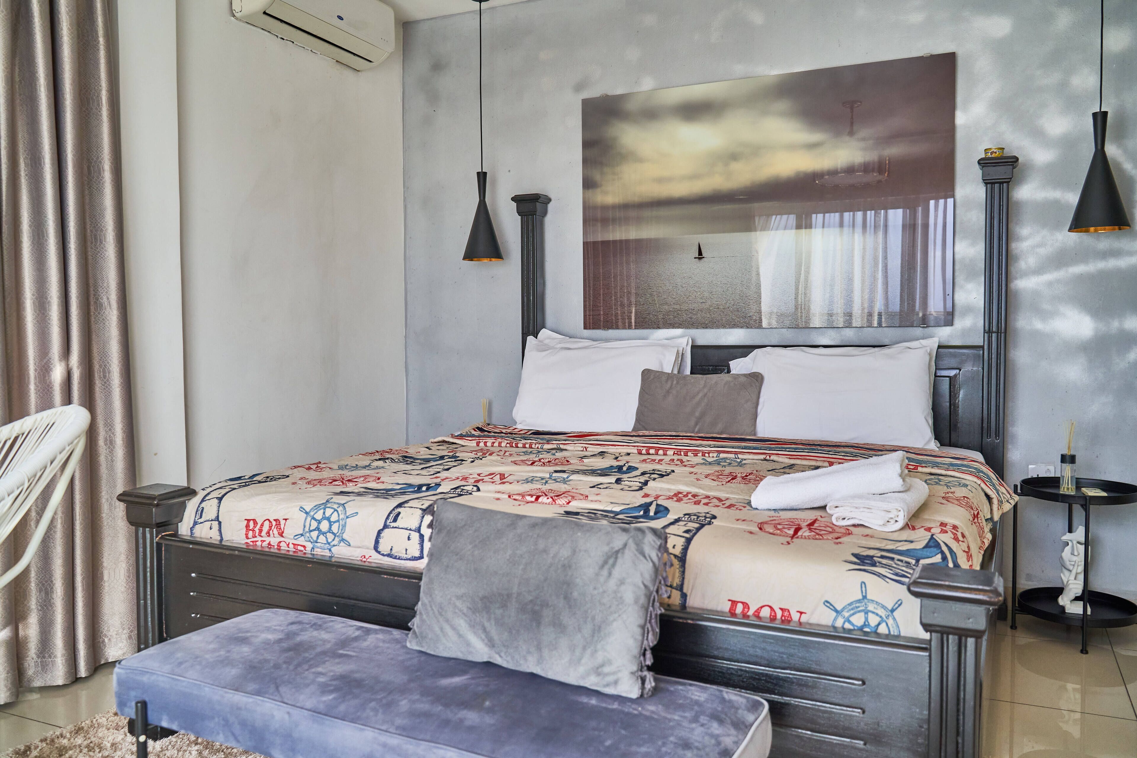Un dormitorio ordenado con cama, mesitas de noche, un banco y una obra de arte colgada en la pared.