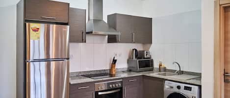 A compact kitchen with a stainless steel refrigerator, built-in oven, microwave, and washing machine.