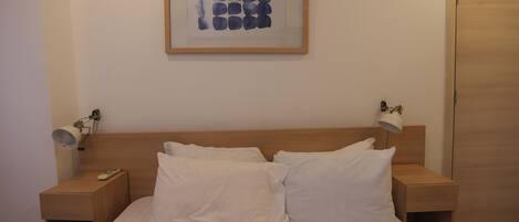 A neatly made bed with white linens and pillows, a framed artwork above it, and bedside lamps on wooden nightstands.