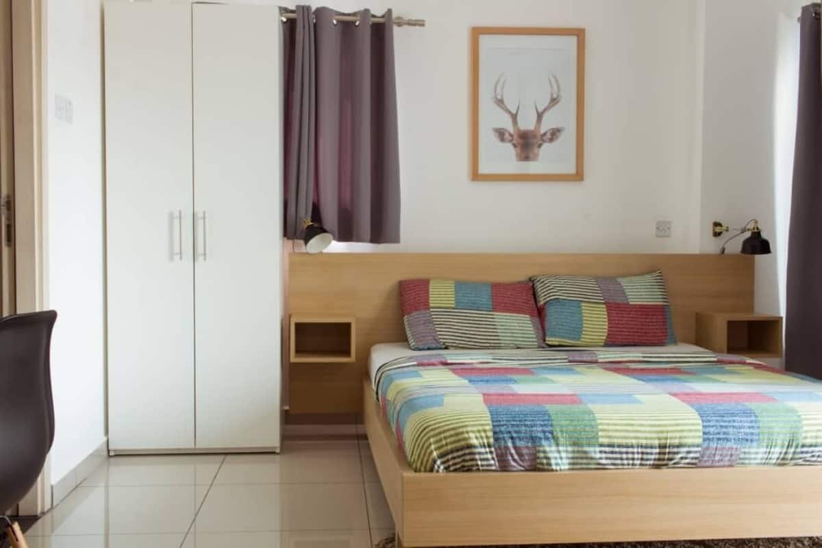A bedroom with a bed, a wardrobe, a desk, and a framed deer head picture on the wall.