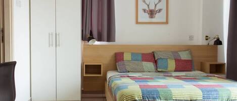 A bedroom with a bed, a wardrobe, a desk, and a framed deer head picture on the wall.