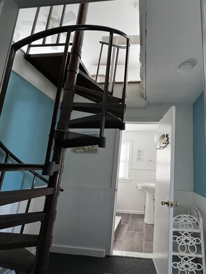 Una escalera de caracol conduce a un piso superior, con vistas a un baño y una puerta blanca con un tirador metálico decorativo.
