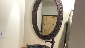 A bathroom with a wooden vanity, a black basin, a mirror with an ornate frame, and shelves with folded towels. - Newly Restored Vintage Cabin near Bryce, Grand Staircase. Great views! (Henrieville)