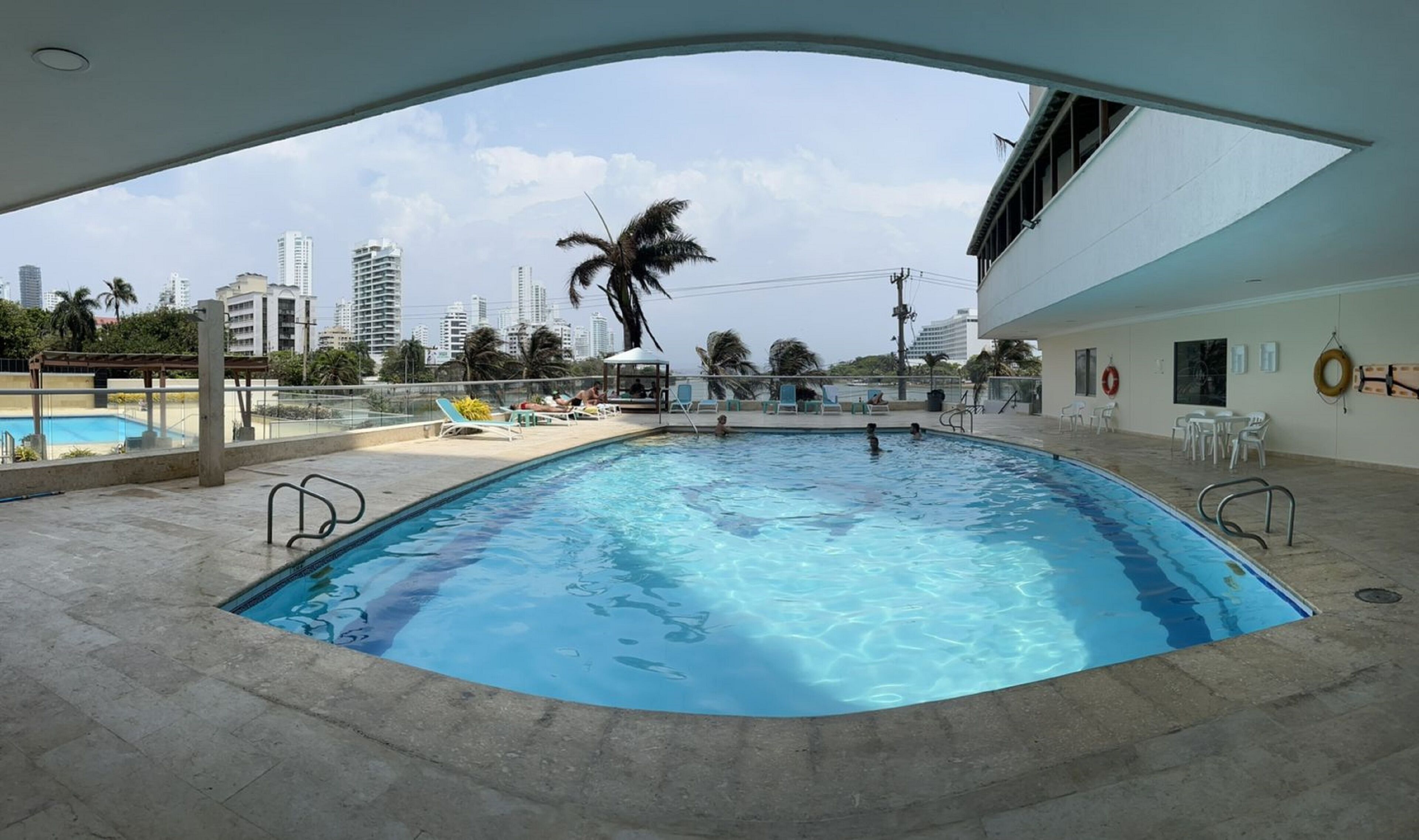 Une piscine intérieure à l’eau cristalline, entourée de chaises longues et offrant une vue sur le paysage urbain.