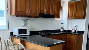 Cozinha com armários de madeira, bancada preta, ilha integrada com banquetas, micro-ondas, fogão e liquidificador.