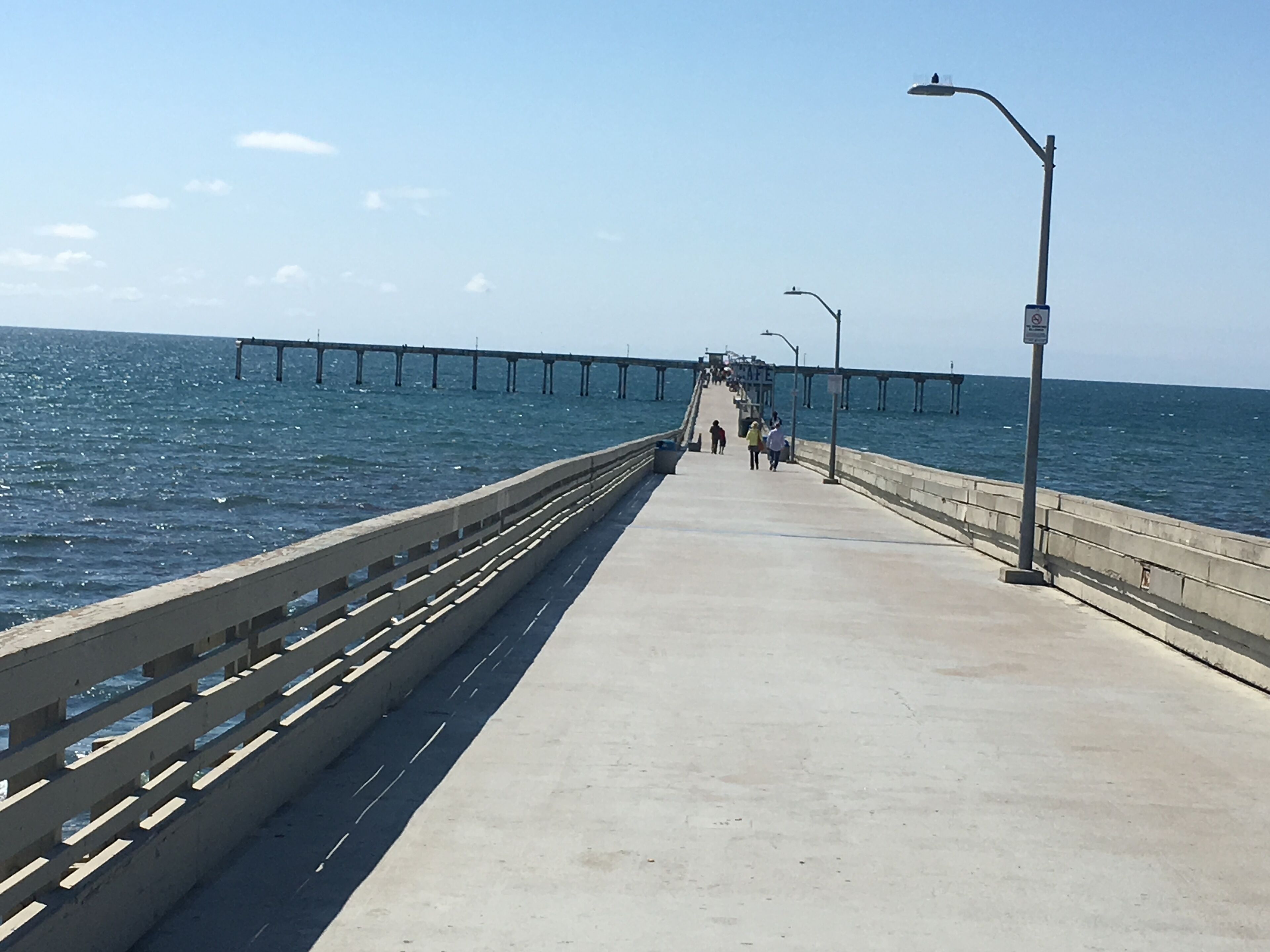 A pier extending into the water with a concrete walkway, railings, and street lamps.