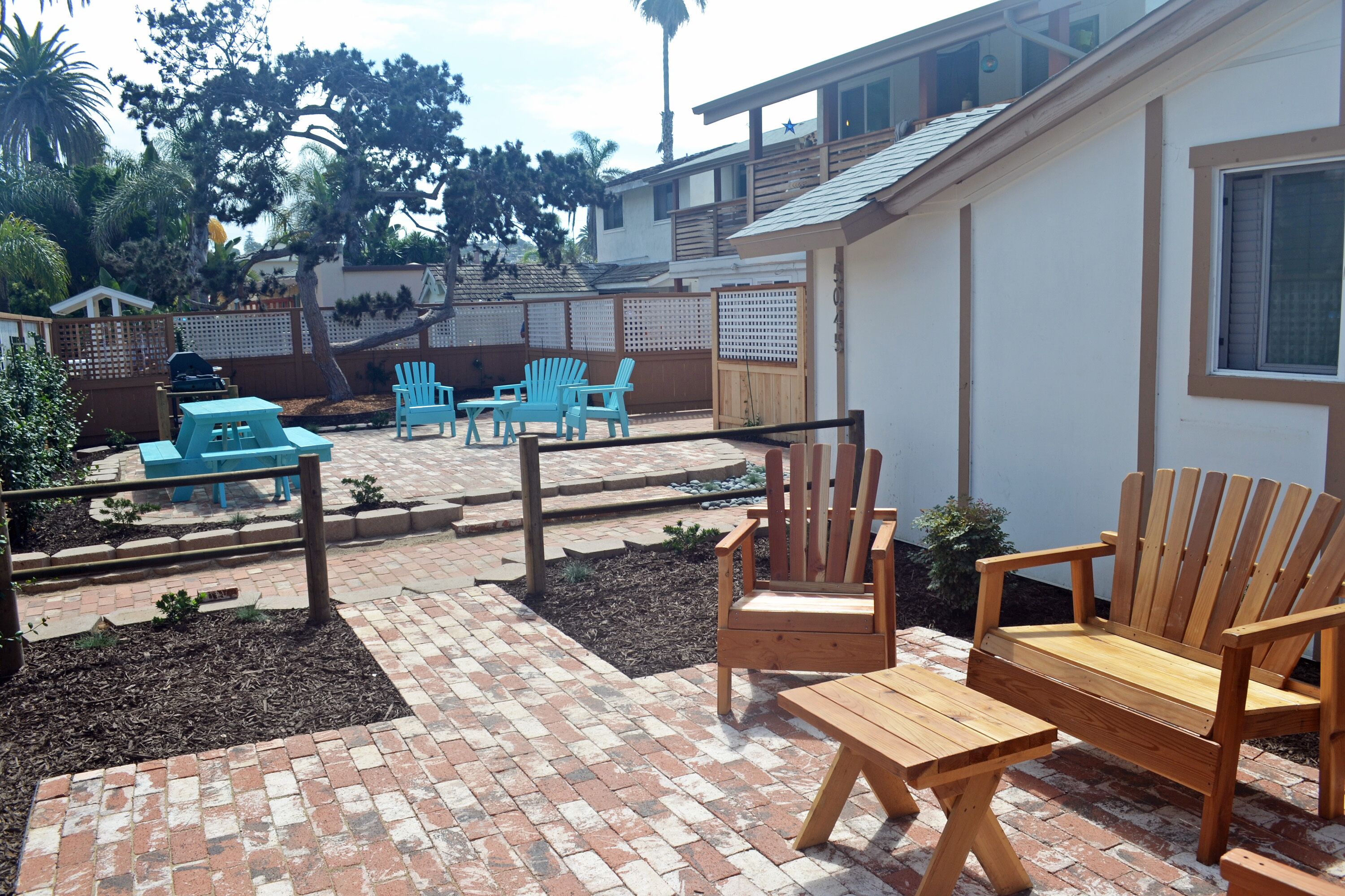 A patio area with wooden furniture, a brick floor, and a view of a residential building.