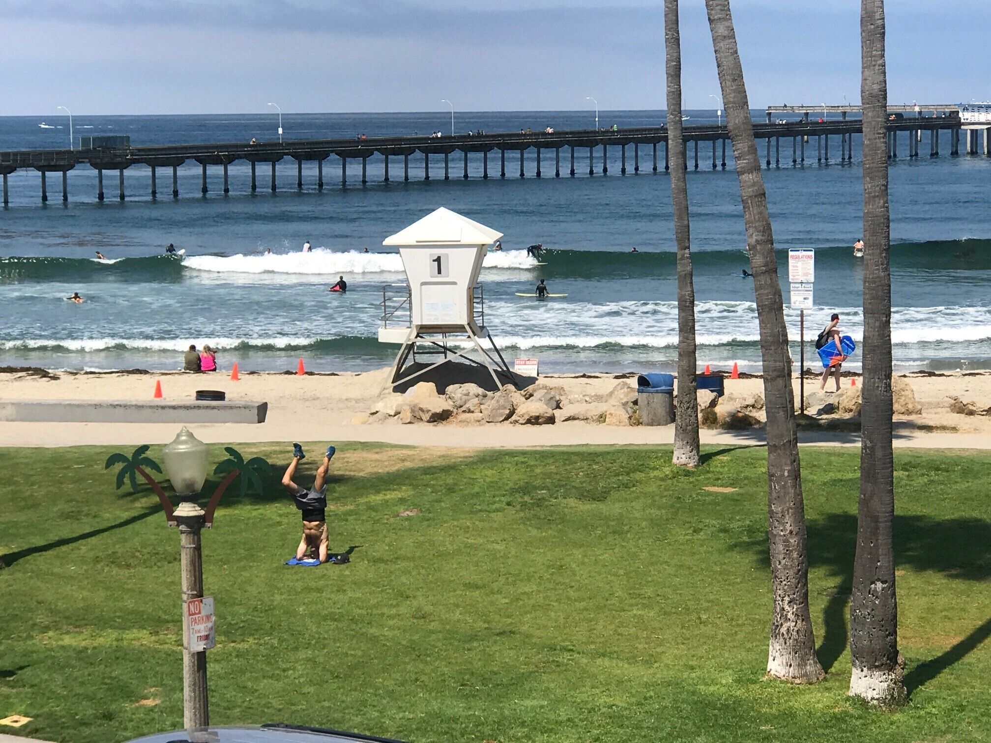 A beach with a lifeguard tower, a pier in the background, and palm trees.