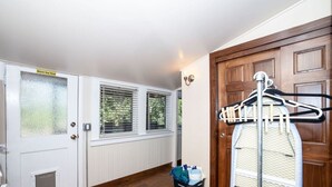 Una habitació amb una porta blanca, una finestra amb persianes, una porta de fusta i un estendal de roba.