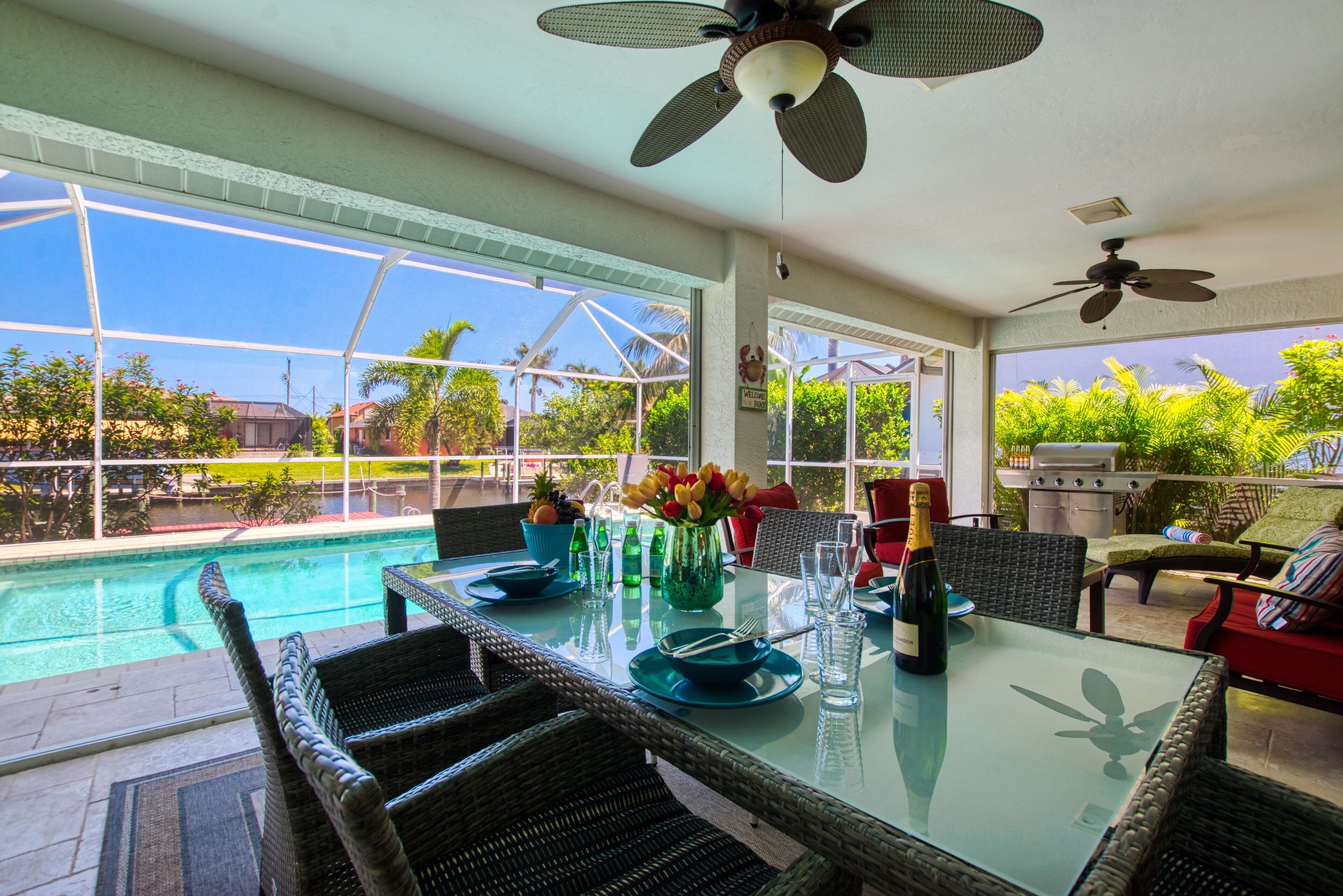A dining area with a glass table, wicker chairs, a pool view, and ceiling fans.