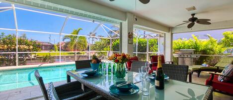 A dining area with a glass table, wicker chairs, a pool view, and ceiling fans.