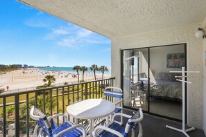 Un balcon donnant sur une plage, une table, des chaises et un lit agrémenté d’un tableau.