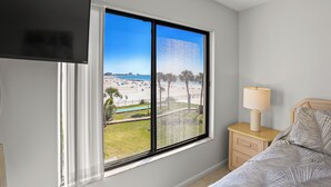 Un dormitorio con un ventanal que ofrece vistas a una playa y palmeras.