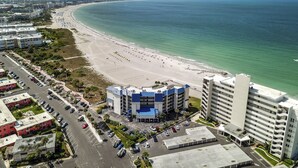 Un hotel frente al mar con vista a la playa, estacionamiento y un edificio grande con techo azul.
