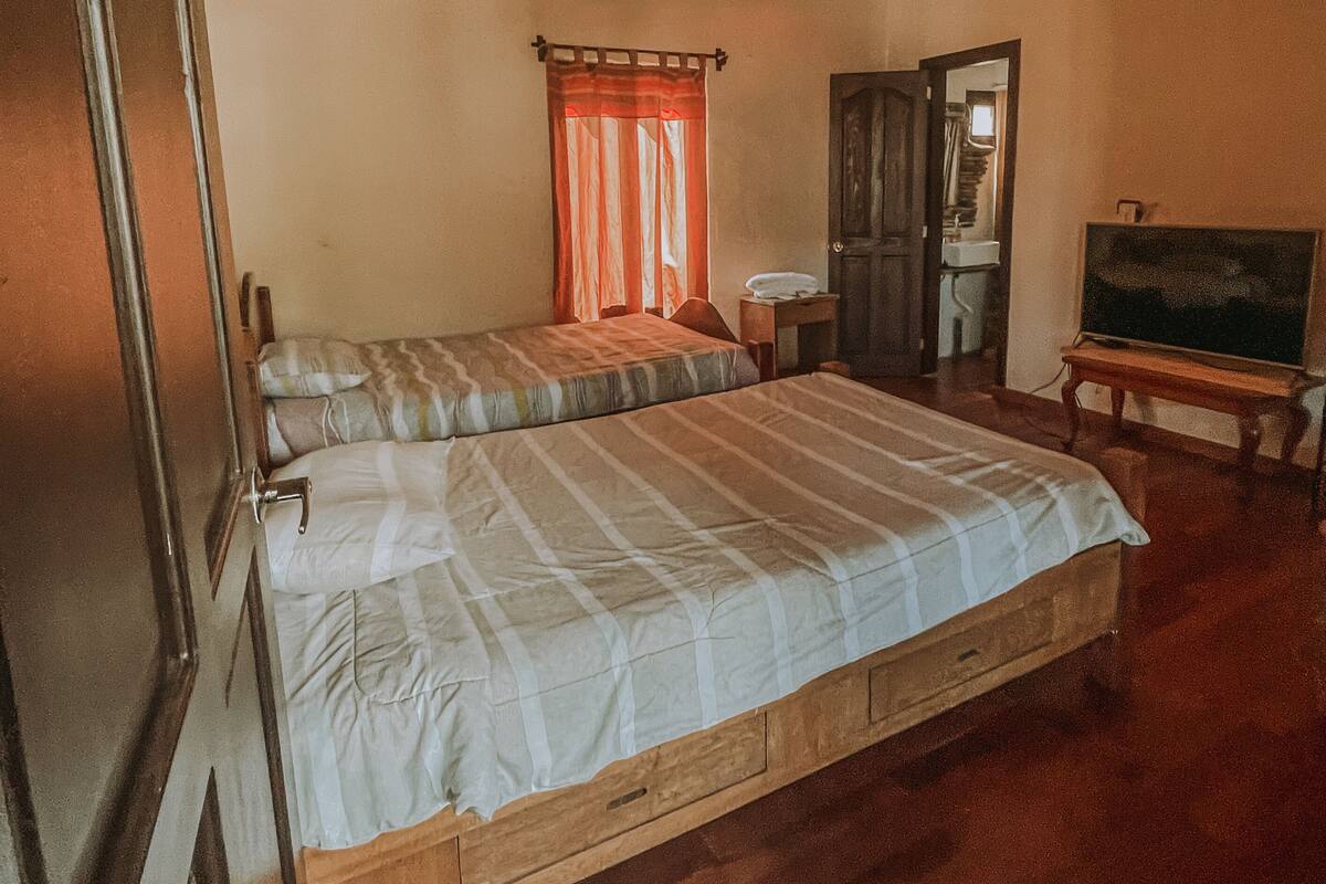 Ein Zimmer mit zwei Holzbett, einem Schrank aus Holz, einem kleinen Tisch und einem Fernseher.