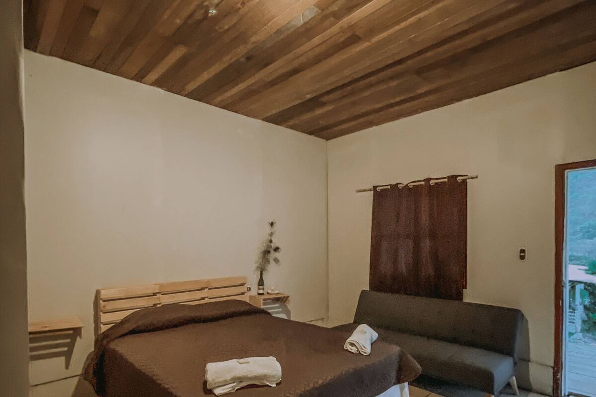 Ein Schlafzimmer mit Holzboden, einem Bett mit brauner Decke, einem grauen Sofa und einem kleinen Tisch mit einer Vase.