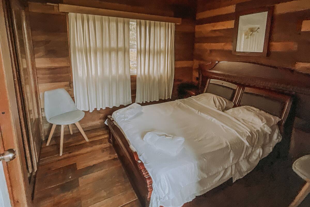 Ein Schlafzimmer einer Holzhütte mit einem Bett, einem Sessel und einem Fenster mit Vorhängen.