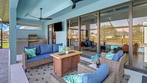 A modern outdoor living area with a sofa, chairs, a table, and a ceiling fan. - The Palms on Surfside 1004 Modern 4BR Heated Pool Home & Outdoor Kitchen (Cape Coral)