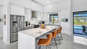 A modern kitchen with a central island, stainless steel appliances, and a view of a swimming pool. - The Palms on Surfside 1004 Modern 4BR Heated Pool Home & Outdoor Kitchen (Cape Coral)