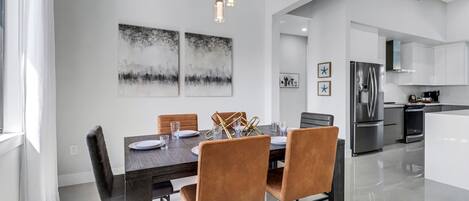 A modern dining area with a dark wooden table, brown upholstered chairs, and two abstract paintings on the wall.