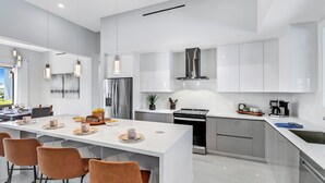 A modern kitchen with white cabinetry, stainless steel appliances, and a central island with seating. - The Palms on Surfside 1004 Modern 4BR Heated Pool Home & Outdoor Kitchen (Cape Coral)
