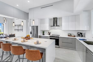 Une cuisine moderne avec des meubles blancs, des appareils en acier inoxydable et un îlot central doté de sièges.