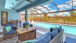 A covered outdoor area with a pool, seating, and a ceiling fan. - The Palms on Surfside 1004 Modern 4BR Heated Pool Home & Outdoor Kitchen (Cape Coral)