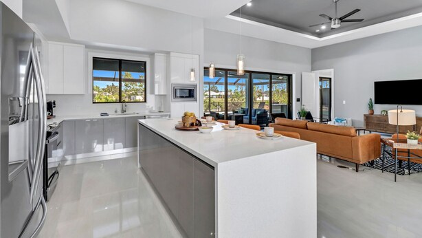 A modern kitchen with a central island, a dining area with a sofa, and a TV. - The Palms on Surfside 1004 Modern 4BR Heated Pool Home & Outdoor Kitchen (Cape Coral)