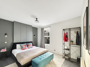 Une chambre à coucher moderne avec un lit, un pouf bleu, une armoire et un miroir.