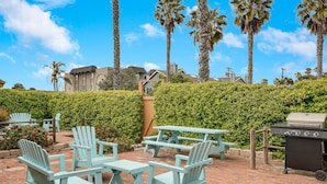 Outdoor seating with Adirondack chairs and picnic tables, a barbecue grill, and a hedge in the background.
