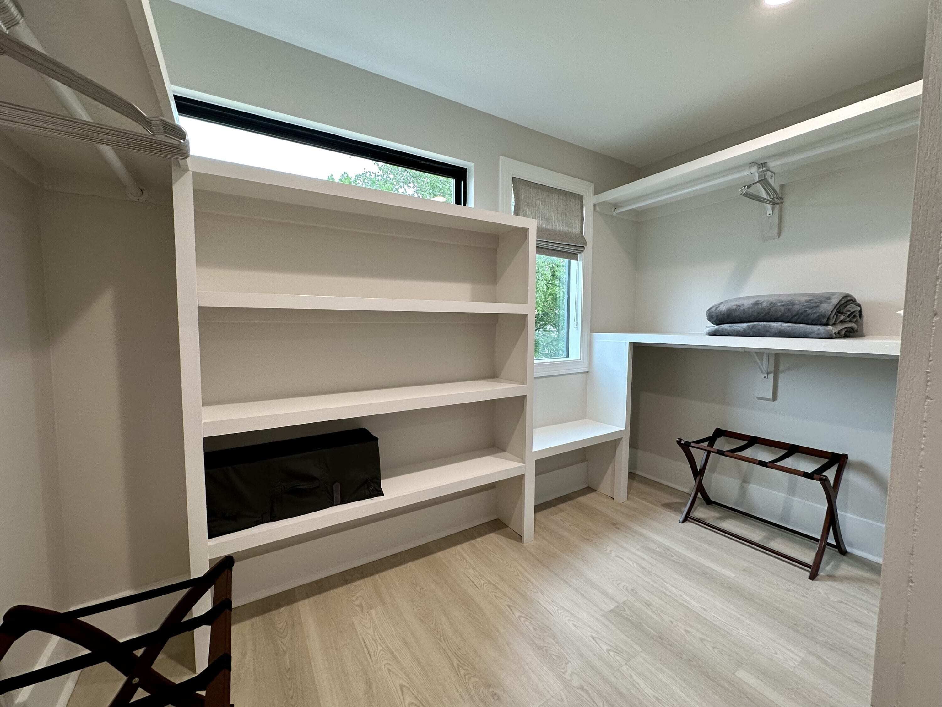 A walk-in closet with white shelving, a small table, and a window.