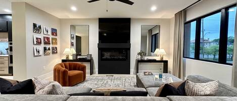 A modern living room with a sofa set, a coffee table, a fireplace, and a ceiling fan.