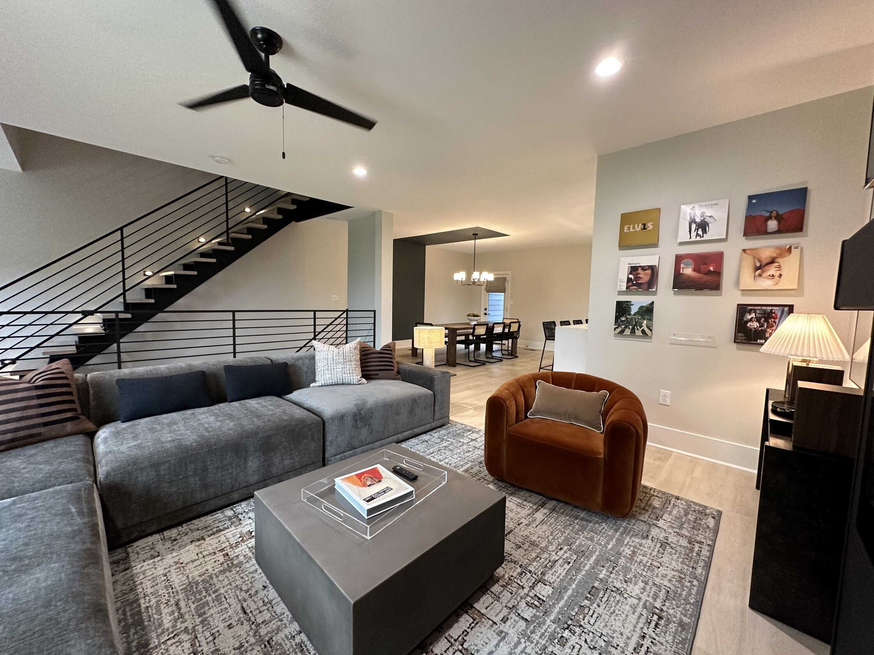 A modern living room with a grey sectional sofa, a brown armchair, a coffee table, and a staircase.