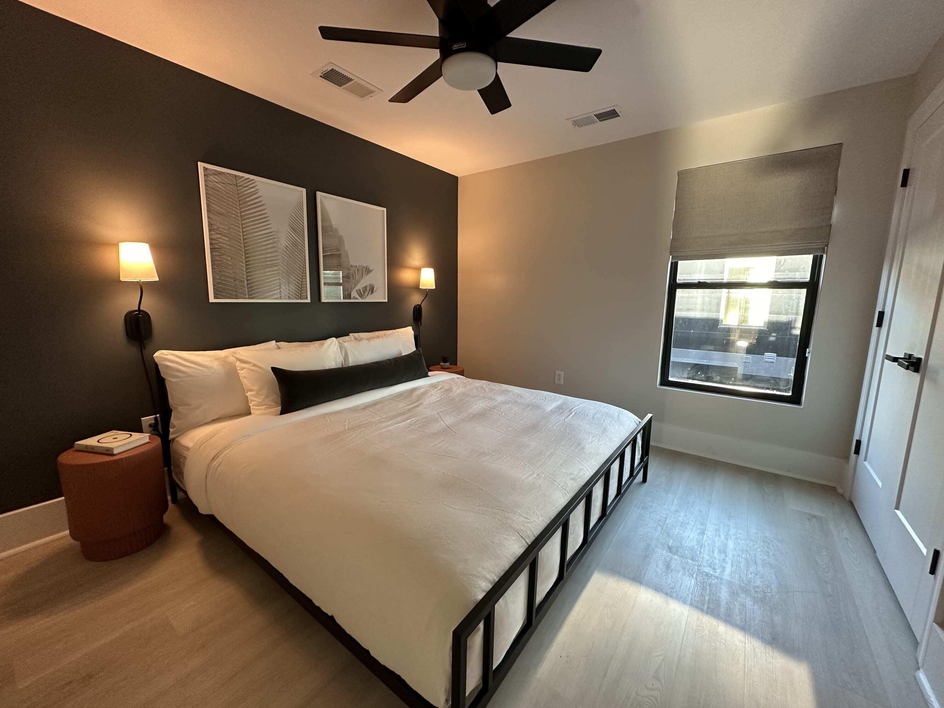 A bedroom with a bed, two bedside lamps, a ceiling fan, and a window with blinds.