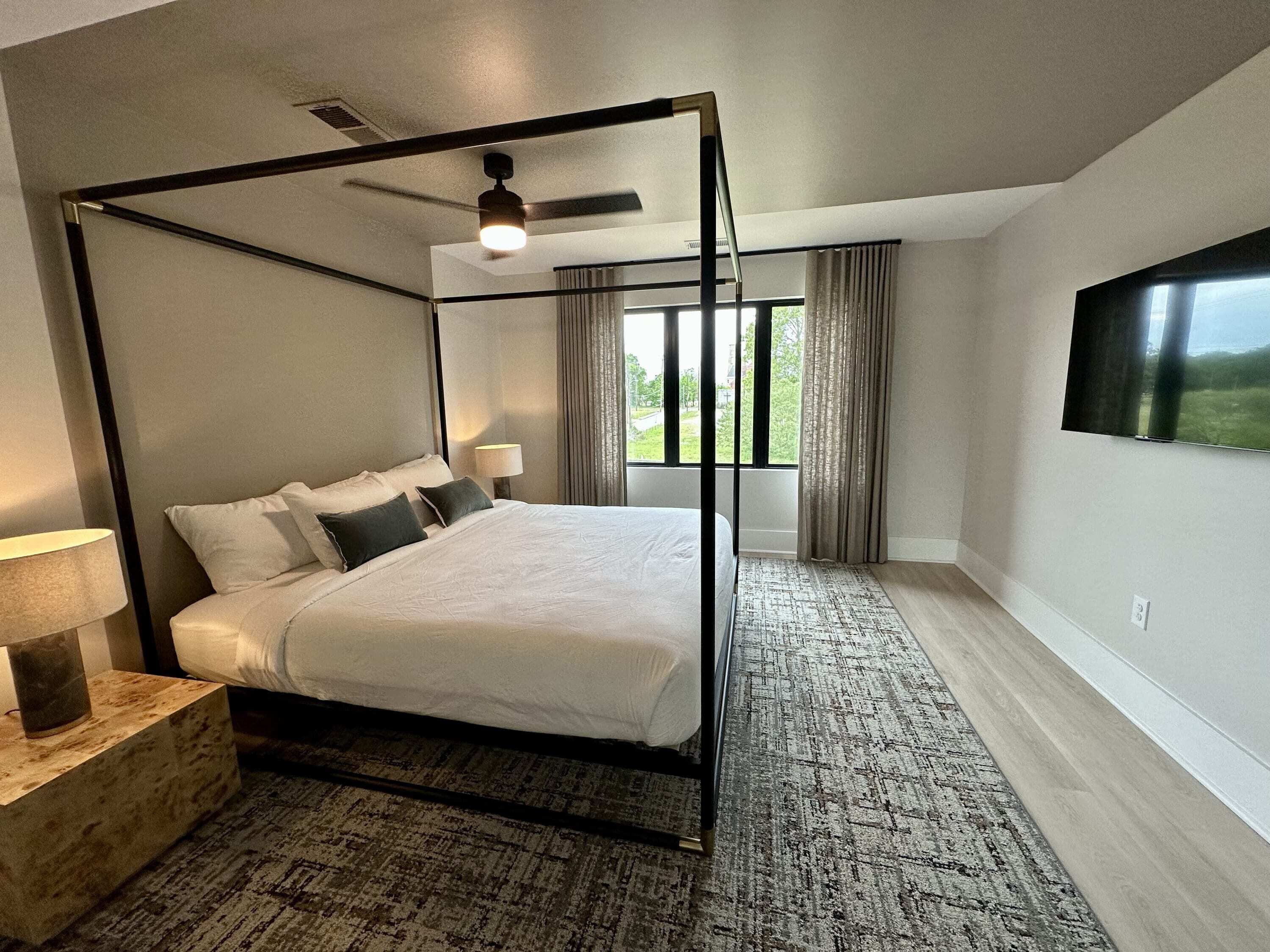 Un lit à baldaquin avec un ventilateur de plafond, un téléviseur fixé au mur et une vue sur la verdure environnante.