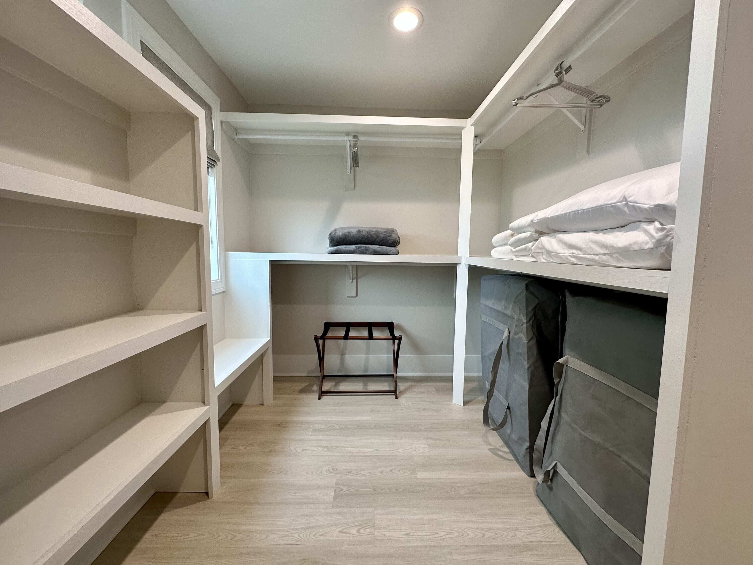 A narrow walk-in closet with wooden flooring, white shelving, and a hanging rack.