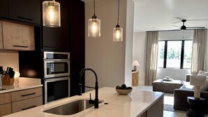 Une cuisine moderne dotée d’un grand îlot central, de fours encastrés et de luminaires suspendus.