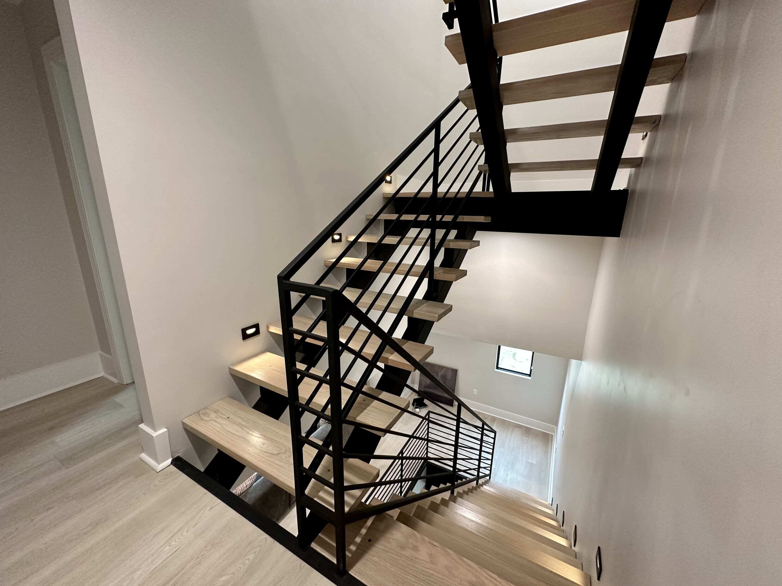 Una escalera moderna con escalones de madera y barandillas de metal negro.