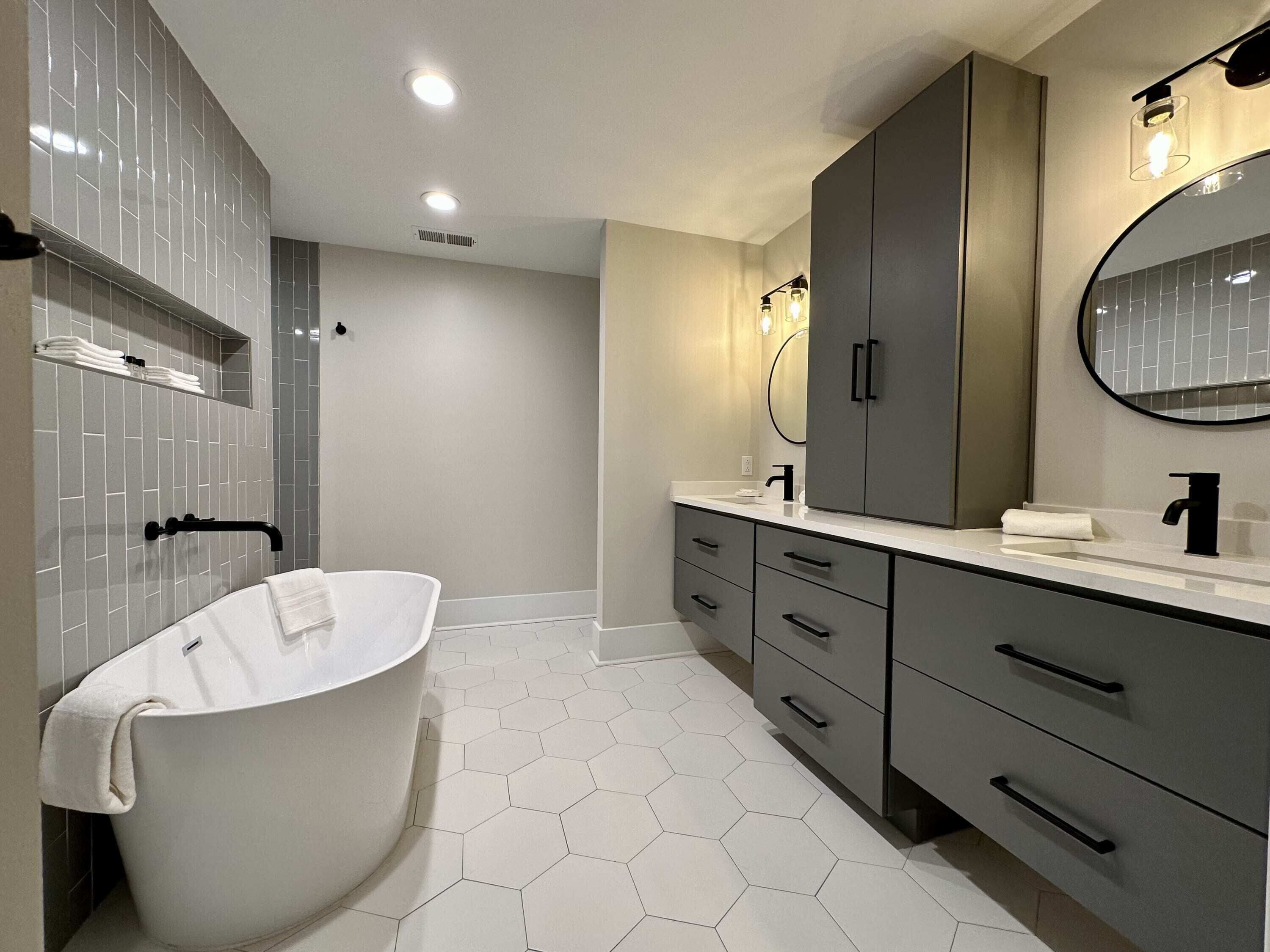 Un baño moderno con una bañera independiente, un espejo grande y un tocador con lavamanos.