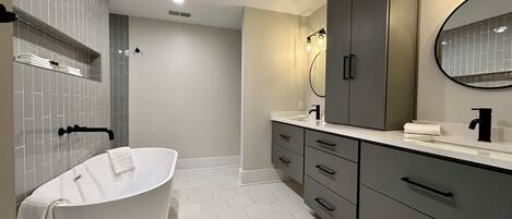 Un baño moderno con una bañera independiente, un espejo grande y un tocador con lavamanos.