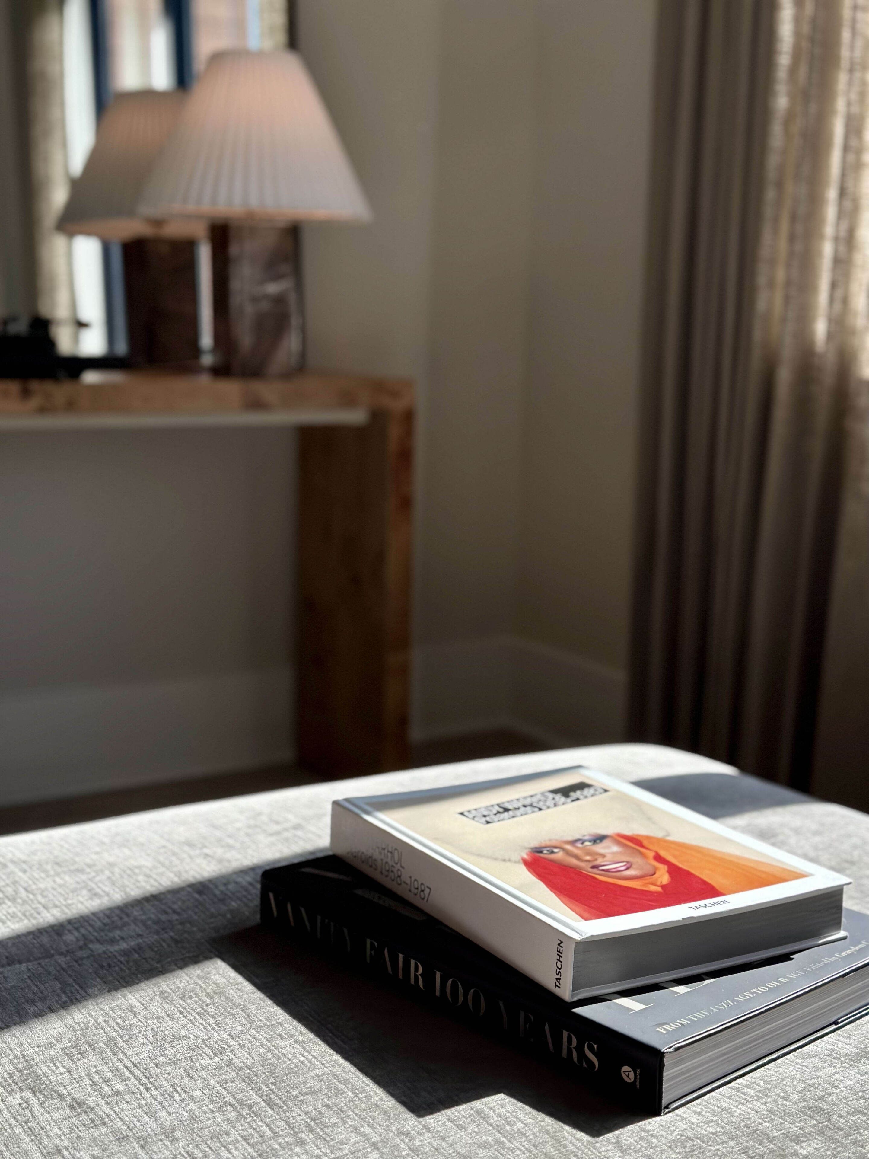 Una pila de libros sobre una mesa, con una lámpara al fondo.
