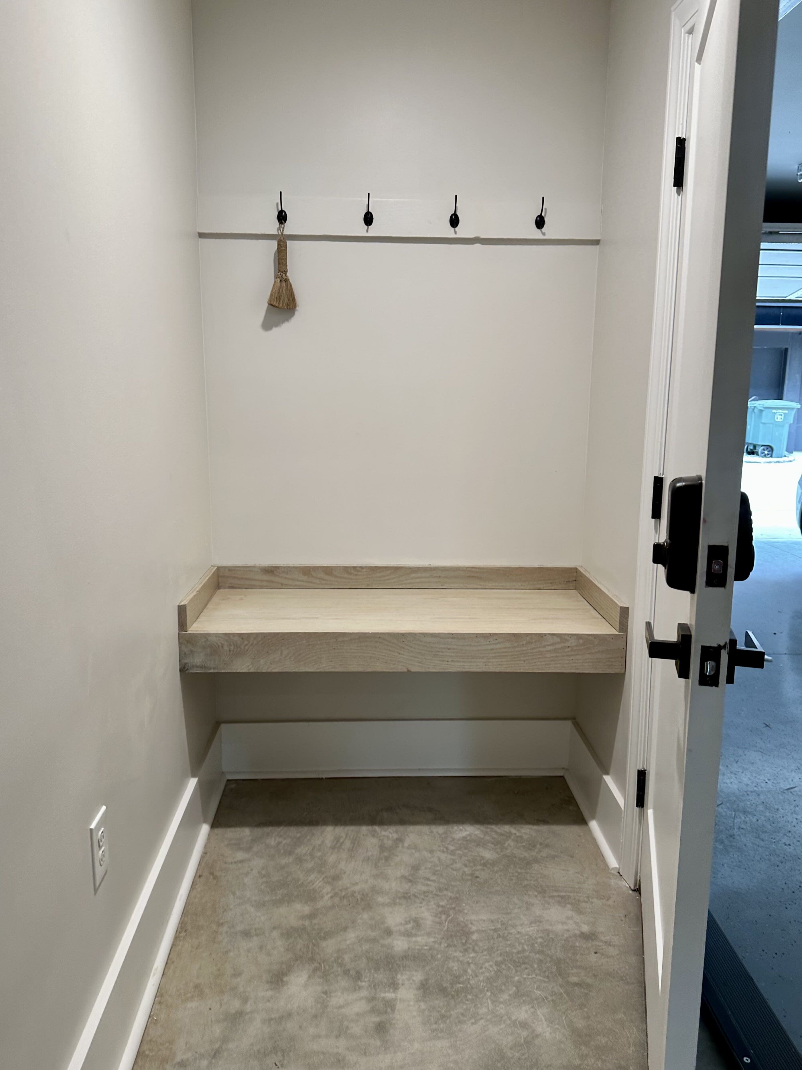 A small, enclosed room with a bench, a coat rack with hooks, and a door leading to an outdoor area.