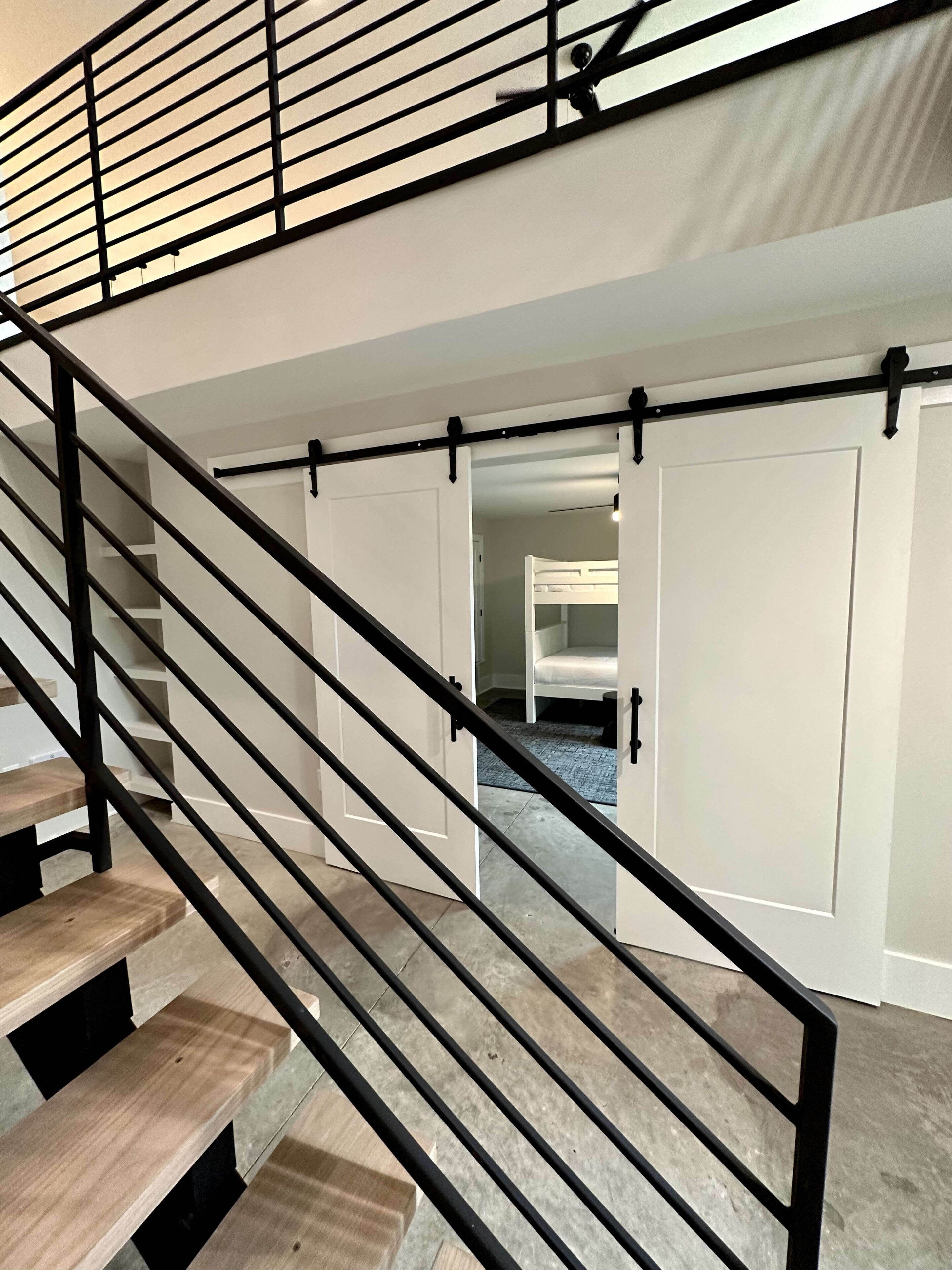 A staircase with black railings leading to a room with white cabinets and a bunk bed.