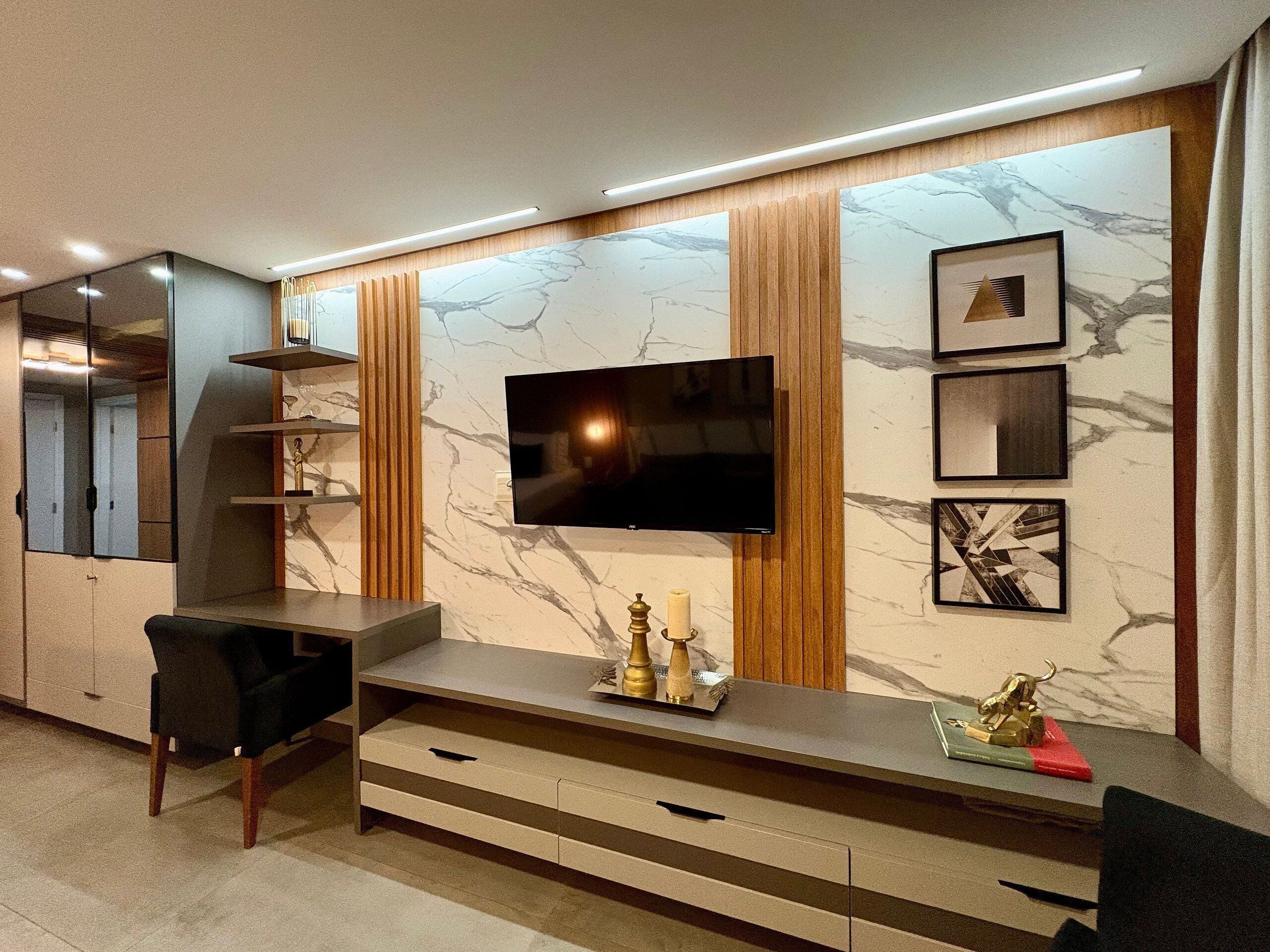 A modern living room with a flat-screen TV, wooden paneling, marble wall, and a desk with drawers.