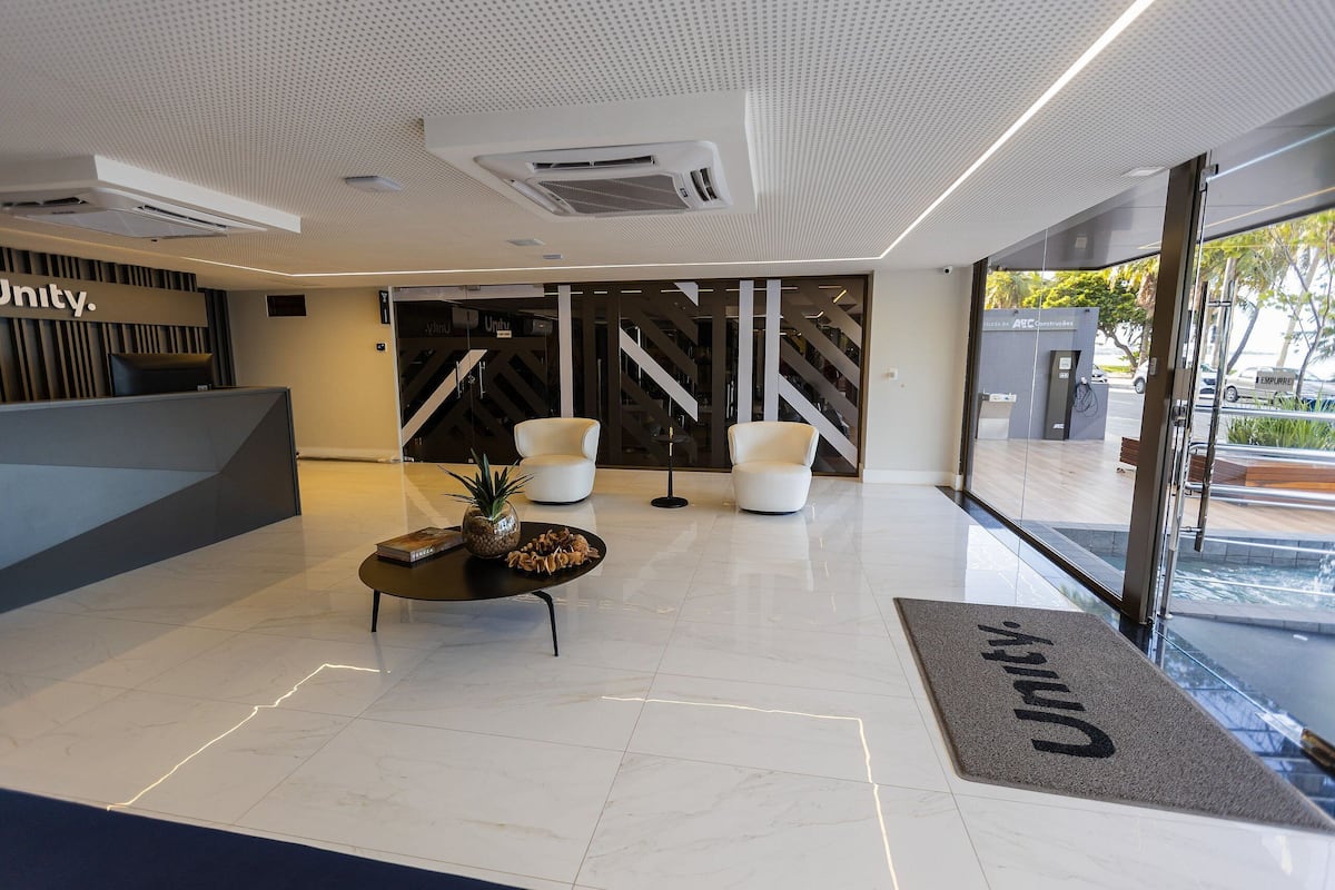 Un área de recepción moderna con mostrador, asientos, una escalera y vistas al exterior.