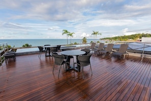 Una terraza de madera con mobiliario exterior, una piscina y vistas al océano.